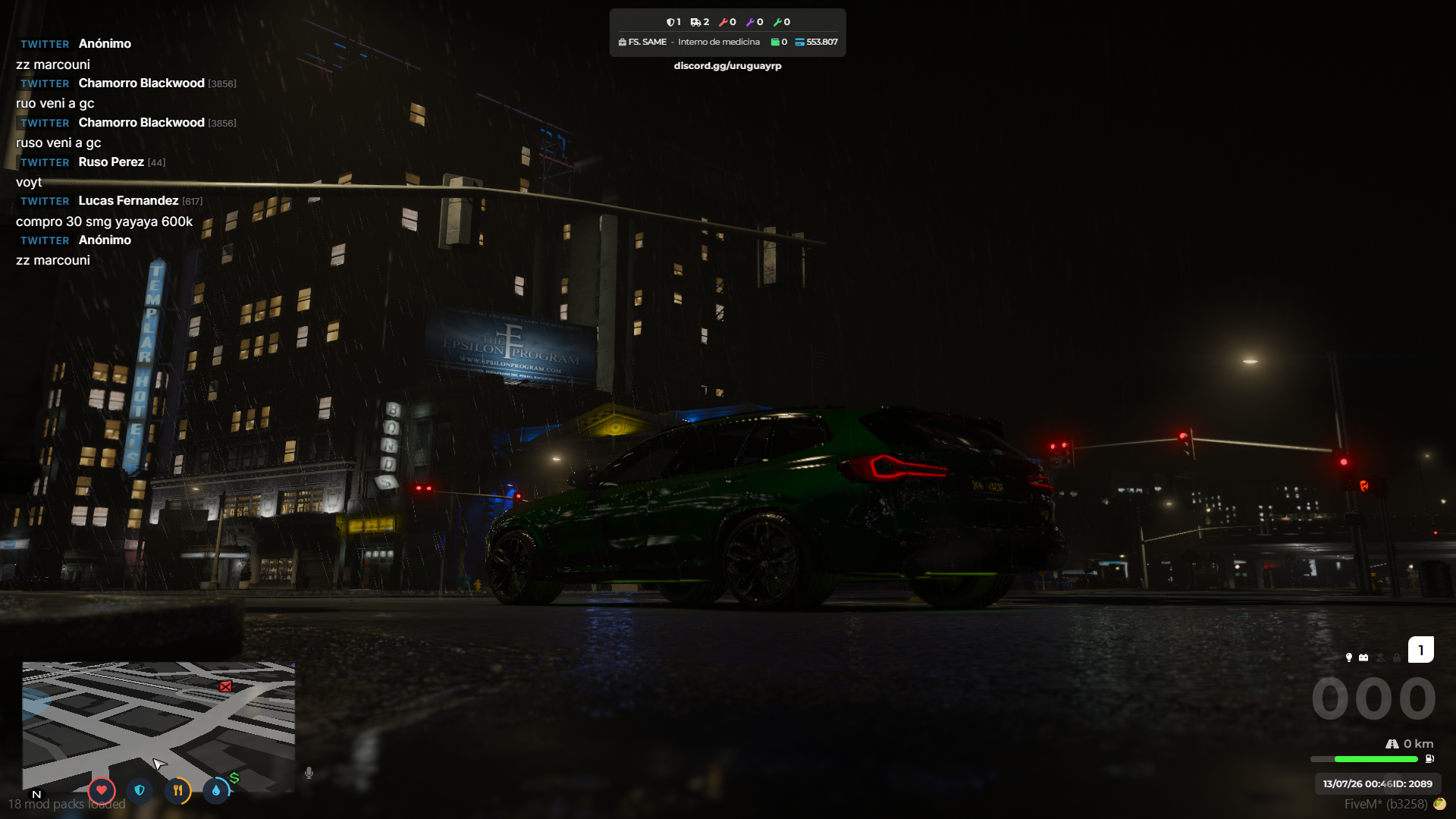 Camioneta BMW verde oscuro en una esquina del centro de noche, bajo la lluvia y entre semáforos en rojo